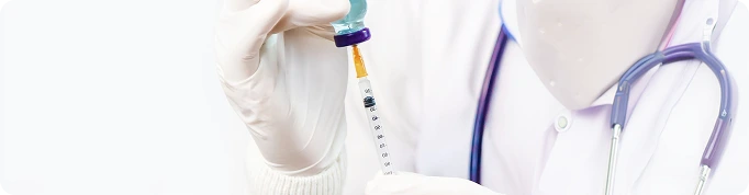 A close-up of a healthcare professional in a white lab coat with a stethoscope, holding a vial and a syringe to draw medication.