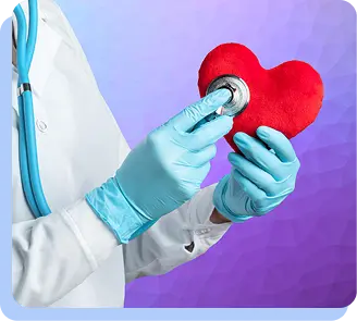 A person wearing blue medical gloves holding a small red heart model and placing a stethoscope chest piece against it.