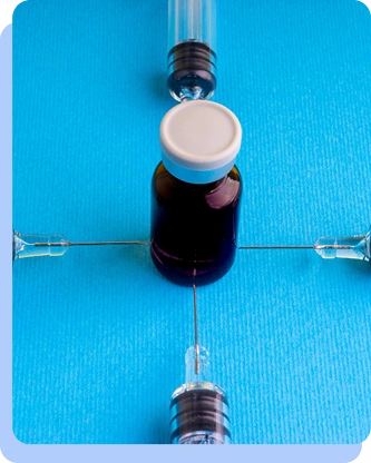 A top-down artistic shot of a small purple medicine vial centered between four syringes pointing toward it on a bright blue background.