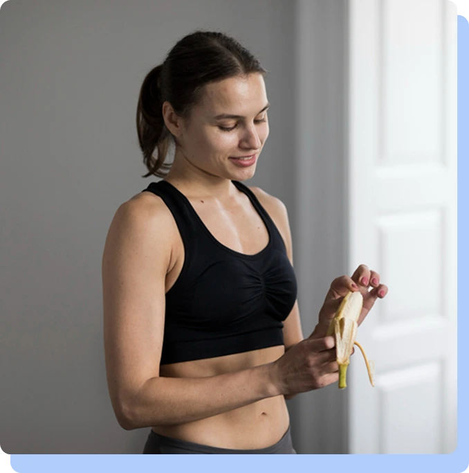 A woman in athletic wear smiling while peeling a banana, representing the combination of healthy lifestyle choices and medical treatment.