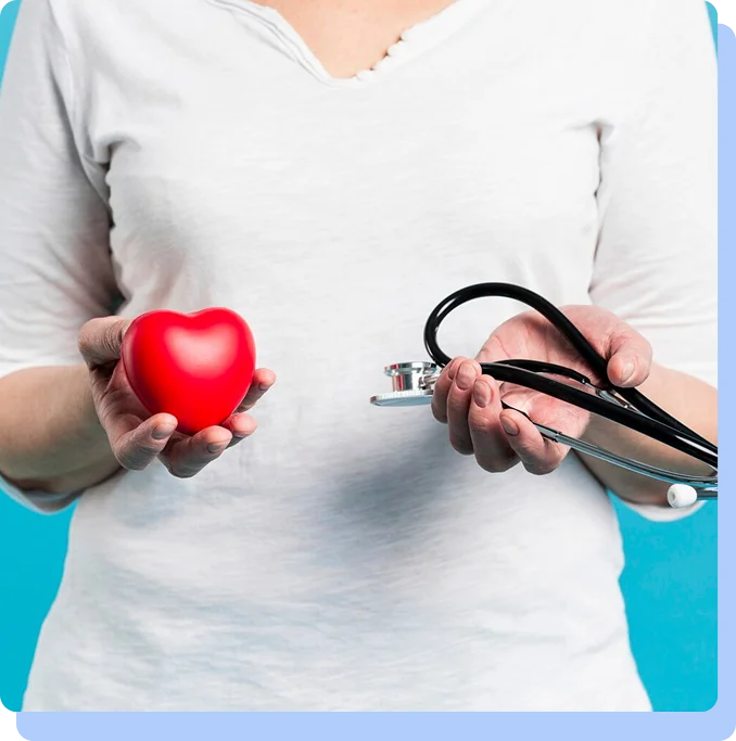 A person in a white shirt holding a small red heart model in their right hand and a black stethoscope in their left hand against a bright blue background.