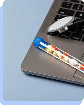 A medical thermometer and a sample tube containing multicolored pills resting on a laptop keyboard.