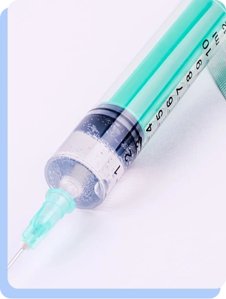 A macro, angled shot of a medical syringe filled with a clear liquid, lying on a plain white surface.