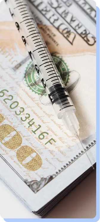 A close-up of a medical syringe lying diagonally across a crisp one-hundred-dollar bill.