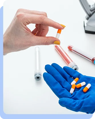 A gloved hand holding several small orange pills while another hand reaches to take one.