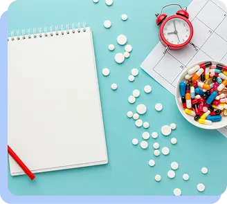 A white notebook next to loose white pills, a red alarm clock, and a bowl of multi-colored capsules.