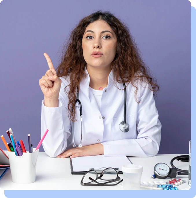 A doctor sitting at a desk with medical tools, holding up an index finger as if providing an important explanation or tip.