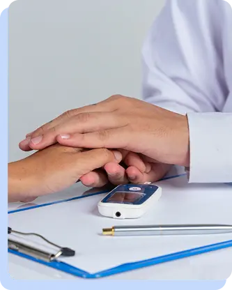 A doctor's hand resting supportively on a patient's hand over a medical clipboard, symbolizing compassionate clinical care.