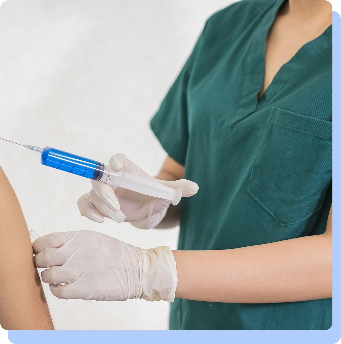 Close-up of a healthcare professional in green scrubs administering an injection into a patient's arm.