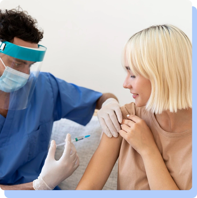 A healthcare worker in a face shield administering an injection into a patient’s upper arm.