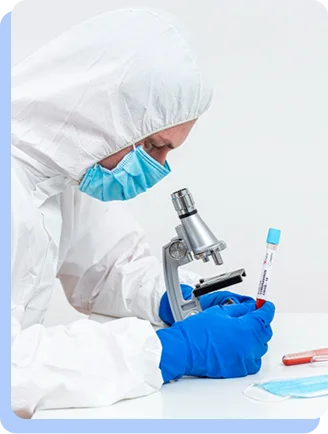 A scientist in a white hazmat suit, mask, and blue gloves looking through a microscope in a laboratory setting.