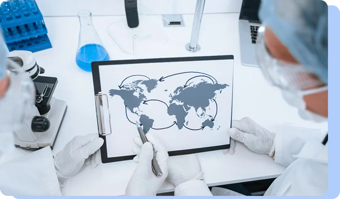Two researchers in white lab coats and protective eyewear look at a clipboard featuring a world map with arrows indicating global connections or data flow.