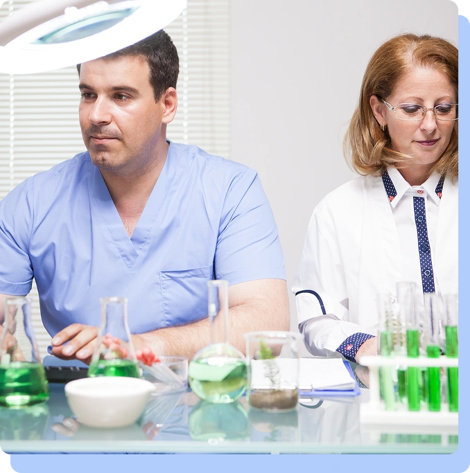 A male and female medical professional working in a laboratory setting with glass flasks and test tubes.
