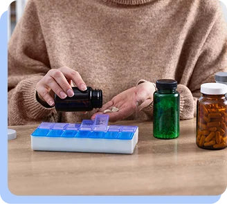 A person sitting at a table organizing various pill bottles and a weekly medication planner.