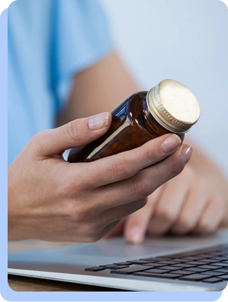 A close-up shot of a person’s hands holding a brown medication bottle over a laptop keyboard, suggesting an online consultation or research.