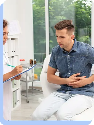 A man in a blue denim shirt sitting in a medical office, looking concerned and holding his side while a healthcare professional in a white coat takes notes on a clipboard.