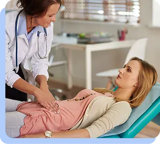 A female doctor in a white lab coat and stethoscope performing a physical examination on a patient lying on an exam table.
