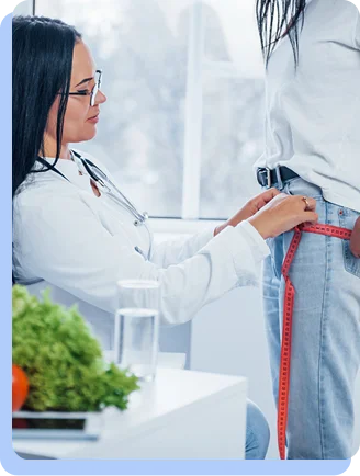 A medical professional in a white lab coat uses a red measuring tape to measure the waistline of a patient.