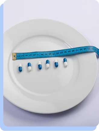 A white plate with several blue and white capsules lined up in a row, with a blue measuring tape draped across them, symbolizing medical weight management.