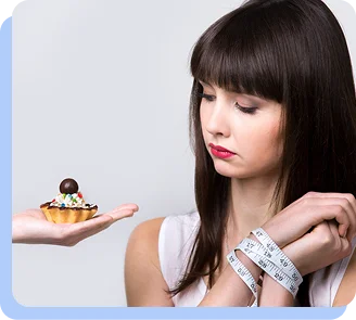 A woman looking down pensively at a small cupcake held in one hand, while a measuring tape is wrapped around her other wrist, illustrating the internal struggle with food choices.