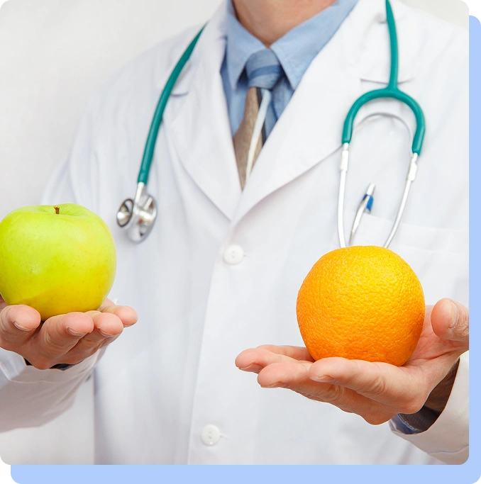 A doctor in a white lab coat with a stethoscope holding a green apple in one hand and an orange in the other.
