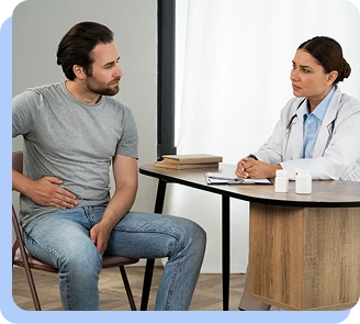 A man in a grey t-shirt sitting on a chair, looking at a doctor while holding his side/lower back, indicating physical discomfort or kidney-area pain.