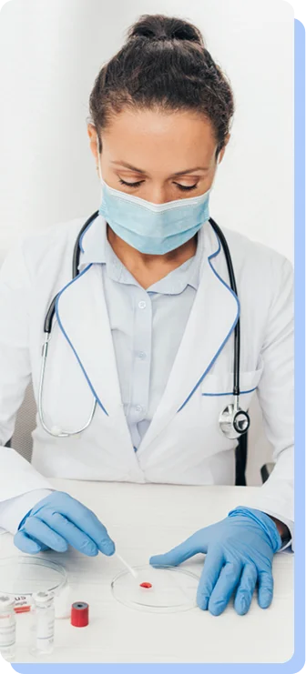 A close-up of a scientist wearing a surgical mask and blue gloves, carefully using a swab to collect a sample from a Petri dish.