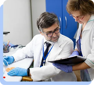 Two researchers in a laboratory setting reviewing documents and clinical data on a desk.