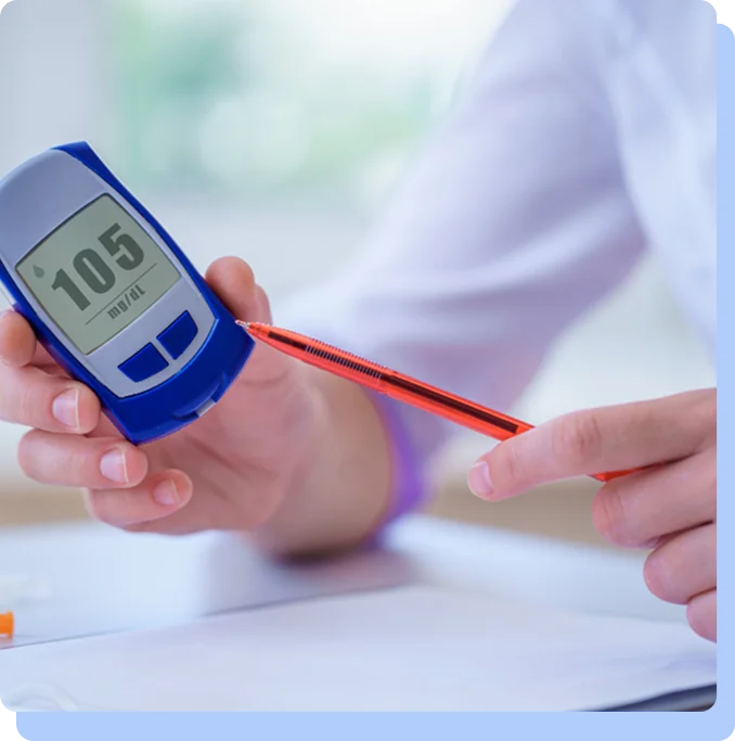 A close-up of a person holding a digital glucose meter displaying a reading of 105, while pointing to the screen with a red pen.