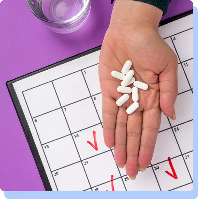 A hand holding several white oblong pills over a monthly calendar with red checkmarks on specific dates.
