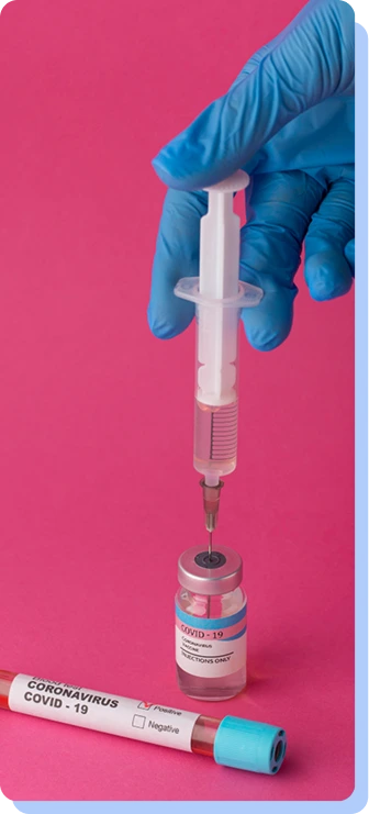 A hand in a blue surgical glove using a syringe to draw liquid from a small medical vial against a pink background.