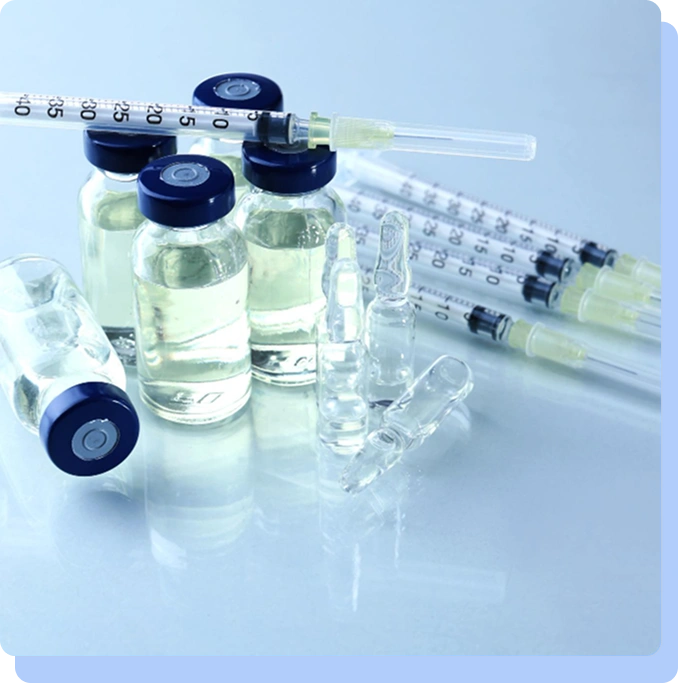A collection of medical supplies including several small glass vials with blue and white caps and multiple clear syringes with needles, arranged on a light surface.