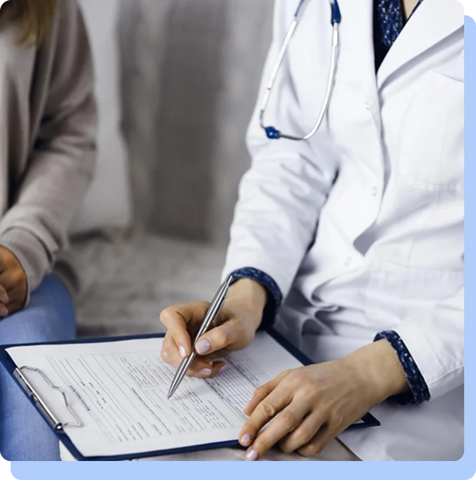 A close-up of a healthcare provider in a white lab coat using a pen to fill out a medical form on a clipboard during a patient consultation.