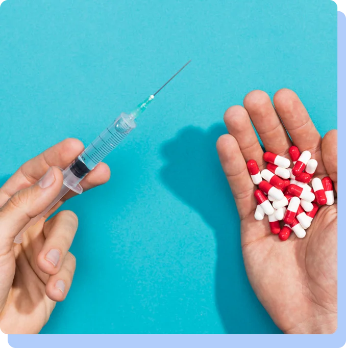 Two hands side-by-side against a blue background; one holds a medical syringe and the other holds a handful of red and white capsules.