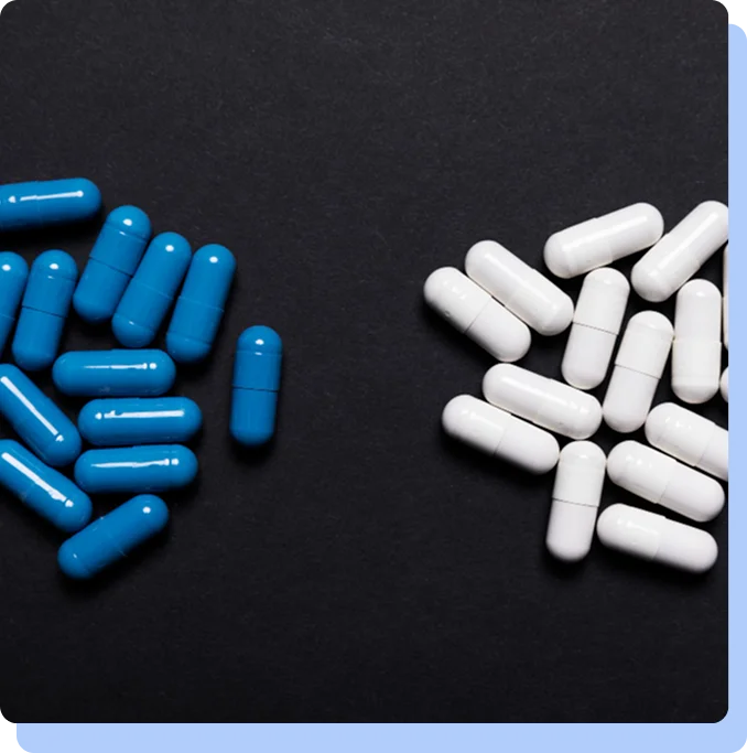 A top-down view of two distinct piles of capsules—blue capsules on the left and white capsules on the right—separated by a dark background.