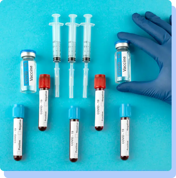 An arrangement of medical supplies on a blue background, including syringes, vaccine vials, and blood sample tubes.